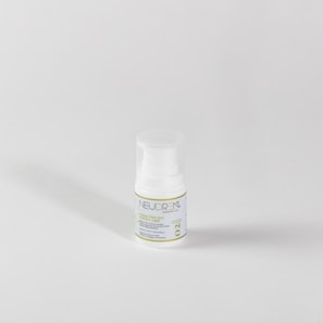 A small white plastic bottle with a pump dispenser sits against a plain light gray background. The bottle features a label with green and blue text, including the word 'NEUDREN'. The lighting creates a soft shadow to the left.