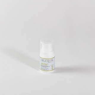 A small white plastic bottle with a pump dispenser sits against a plain light gray background. The bottle features a label with green and blue text, including the word 'NEUDREN'. The lighting creates a soft shadow to the left.