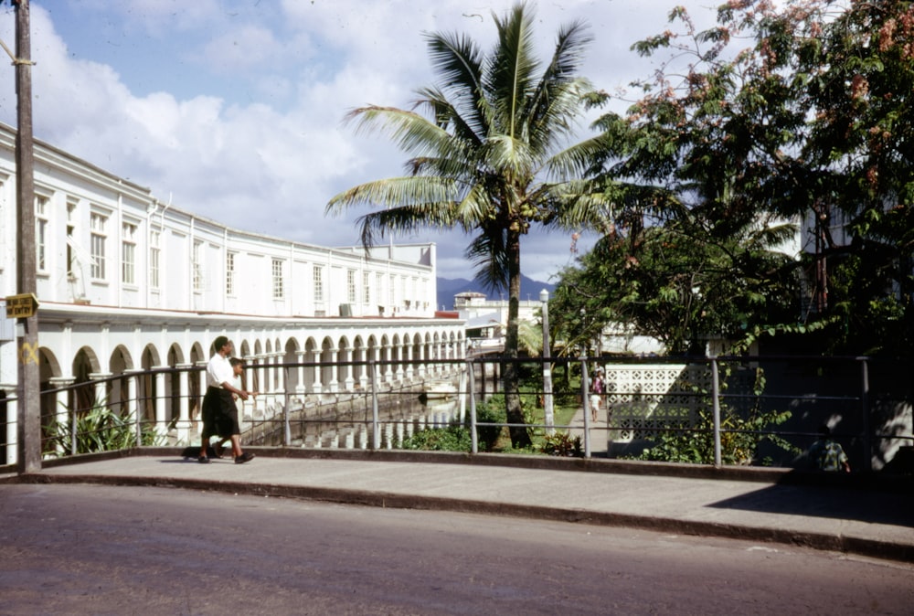 man in black jacket walking on sidewalk near palm trees during daytime