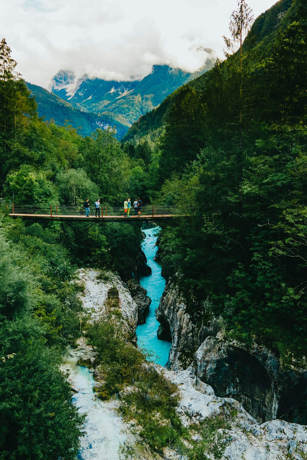 Person in grüner Jacke und schwarzer Hose, die tagsüber auf der Brücke über den Fluss steht