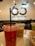 Three plastic cups with drinks are placed on a marble countertop. The focus is on the foreground cup, which contains a vivid red drink. Two cups in the background hold light brown and green drinks. The cups have straws and are branded with the text '65 degrees'. The background is slightly blurred, featuring a large wall sign that repeats the '65 degrees' branding.