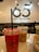 Three plastic cups with drinks are placed on a marble countertop. The focus is on the foreground cup, which contains a vivid red drink. Two cups in the background hold light brown and green drinks. The cups have straws and are branded with the text '65 degrees'. The background is slightly blurred, featuring a large wall sign that repeats the '65 degrees' branding.