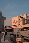 A large building facade with text in red and blue lines, with an industrial vehicle parked in front. The vehicle appears to be a construction or utility truck with machinery attached.