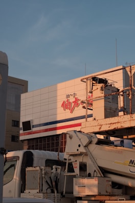A large building facade with text in red and blue lines, with an industrial vehicle parked in front. The vehicle appears to be a construction or utility truck with machinery attached.