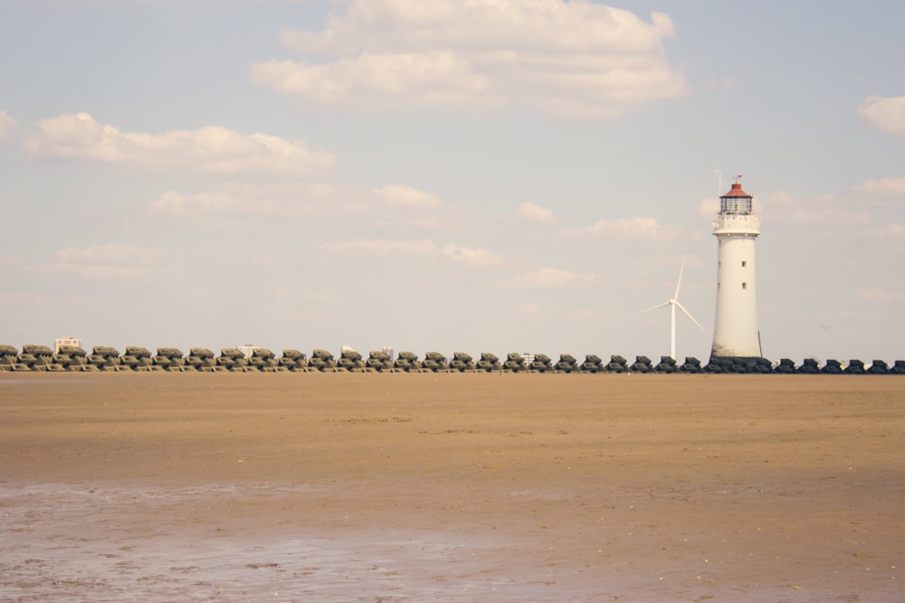 white lighthouse on brown sand near body of water during daytime