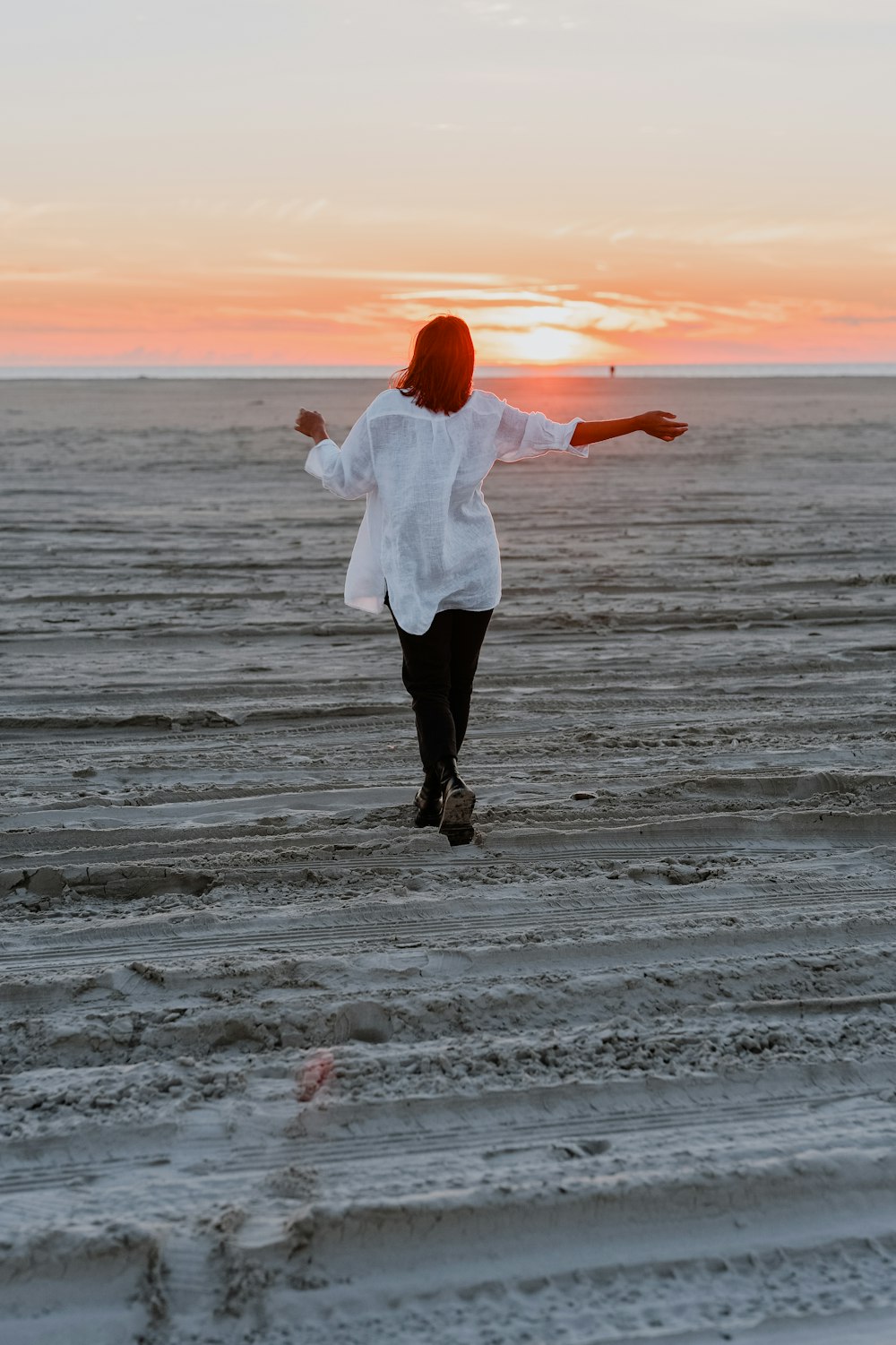 donna in camicia bianca a maniche lunghe e pantaloni neri in piedi sulla spiaggia durante il tramonto