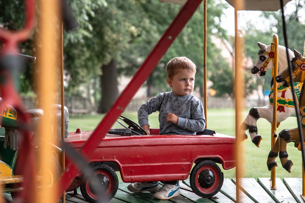 boy in blue long sleeve shirt sitting on red car