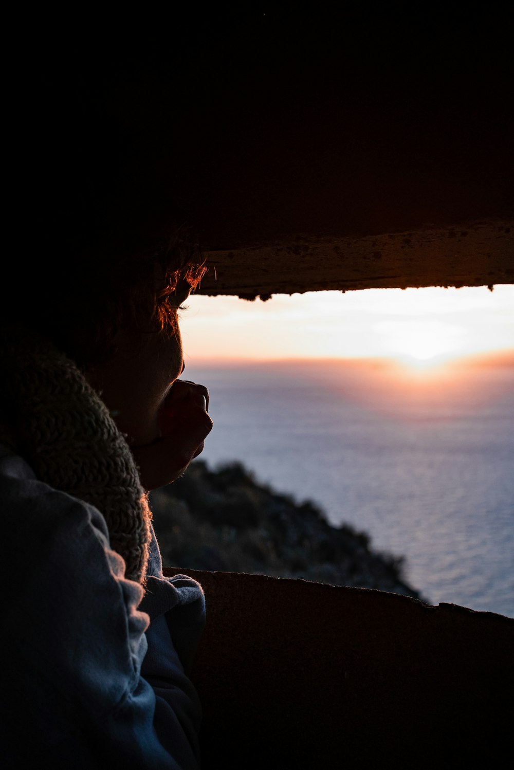 Mujer en pañuelo blanco sentado en la roca durante la puesta del sol