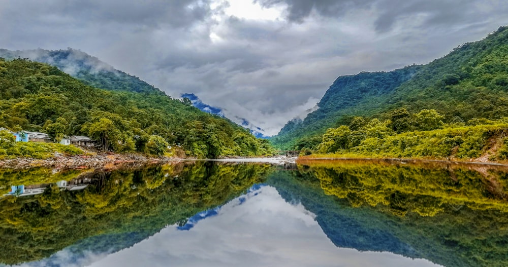 montagna verde accanto allo specchio d'acqua sotto il cielo nuvoloso durante il giorno