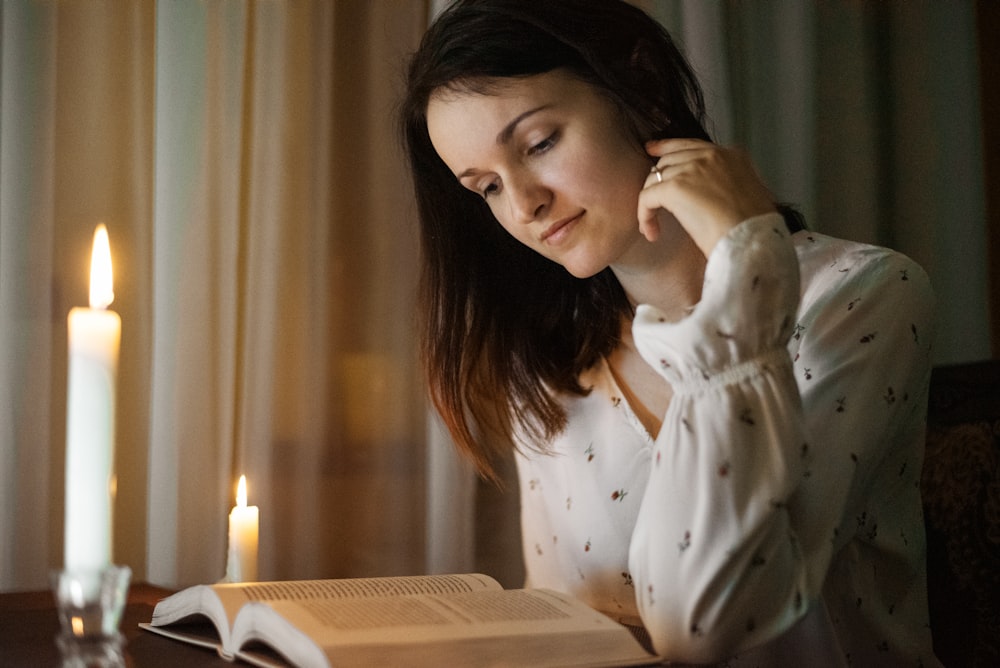 woman in white and red floral long sleeve shirt sitting by the table with lighted candles