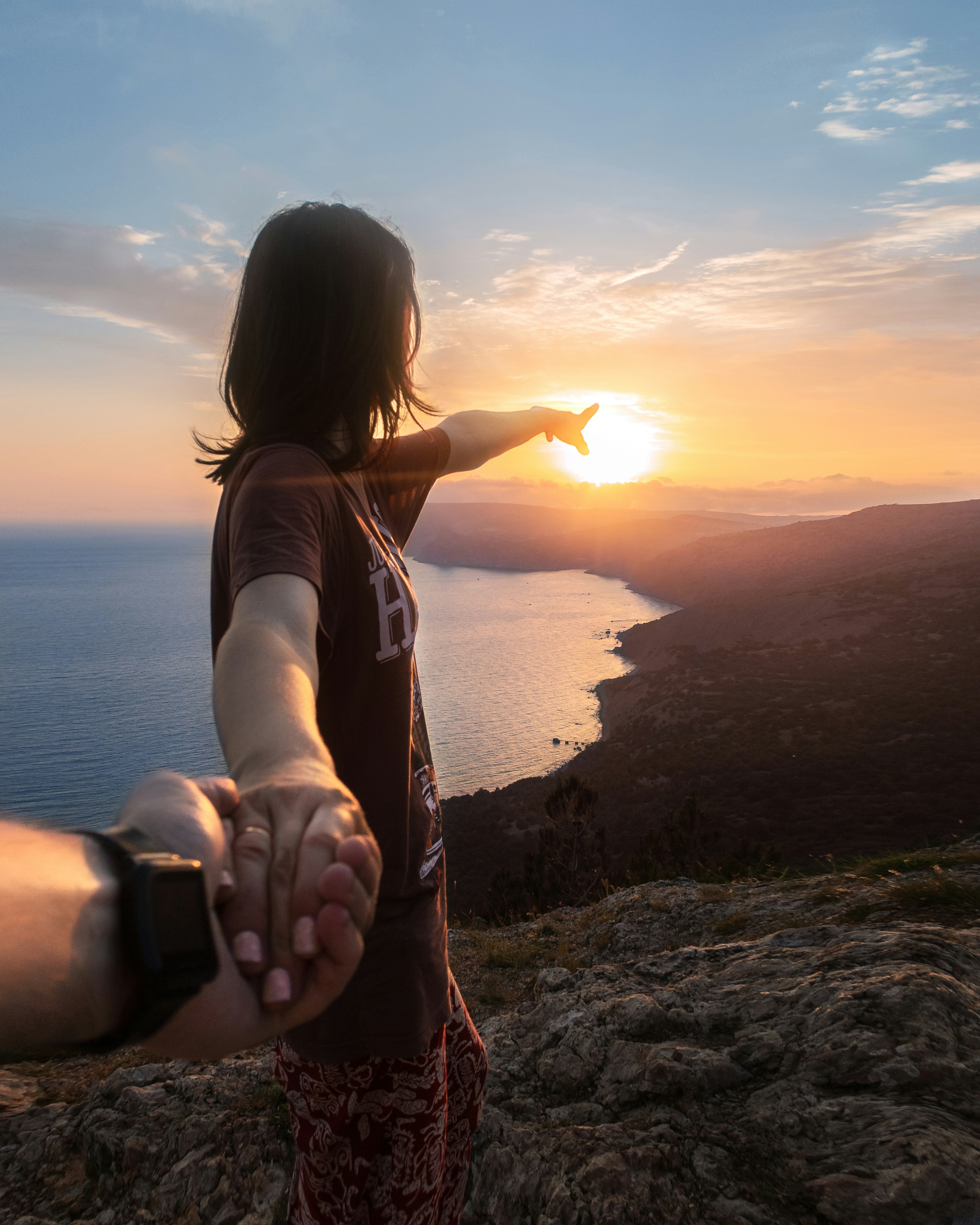 woman in white tank top sitting on rock during sunset