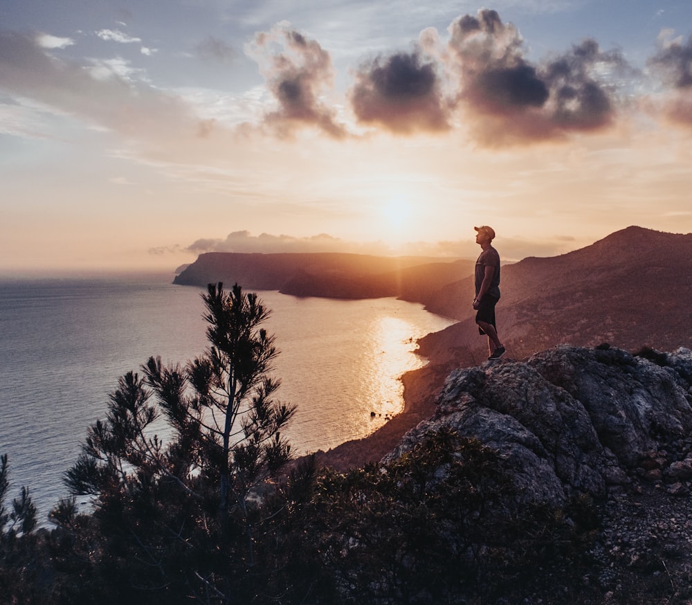man standing on rock near body of water during sunset