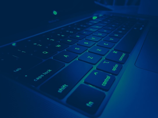 A close-up view of a laptop keyboard with backlit keys. The image uses a blue-green color filter, creating a futuristic and tech-oriented feel. The keys are clearly visible, including function keys, arrows, and standard letter keys.