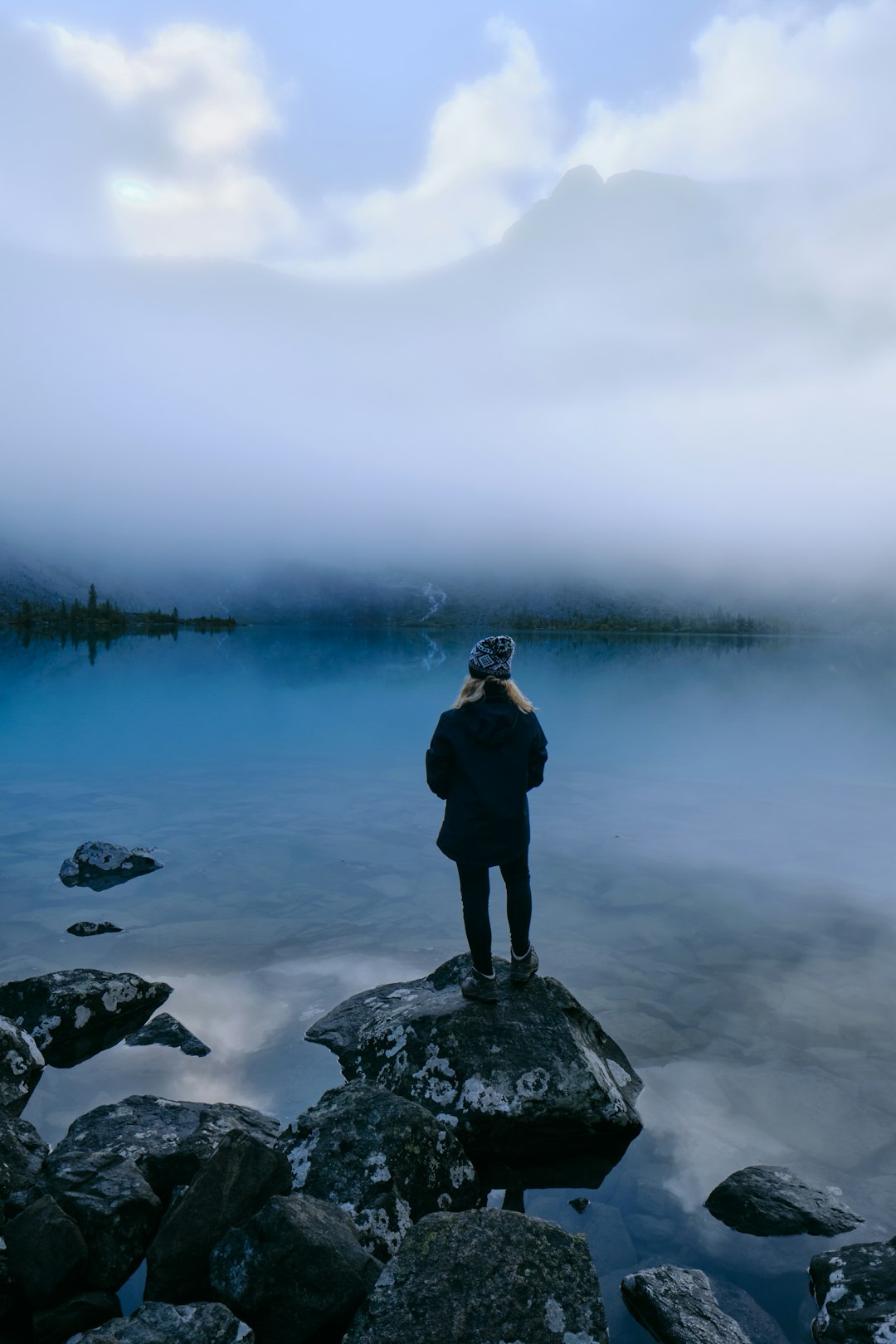 man in black jacket standing on rock near body of water during daytime