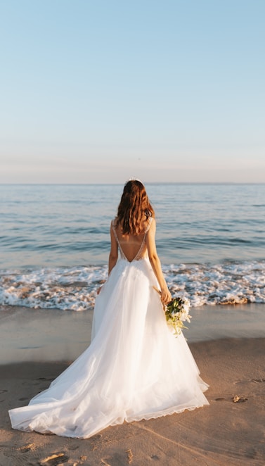 woman in white wedding dress standing on beach during daytime