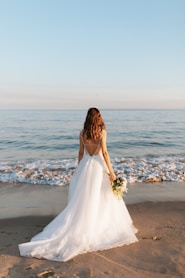 woman in white wedding dress standing on beach during daytime