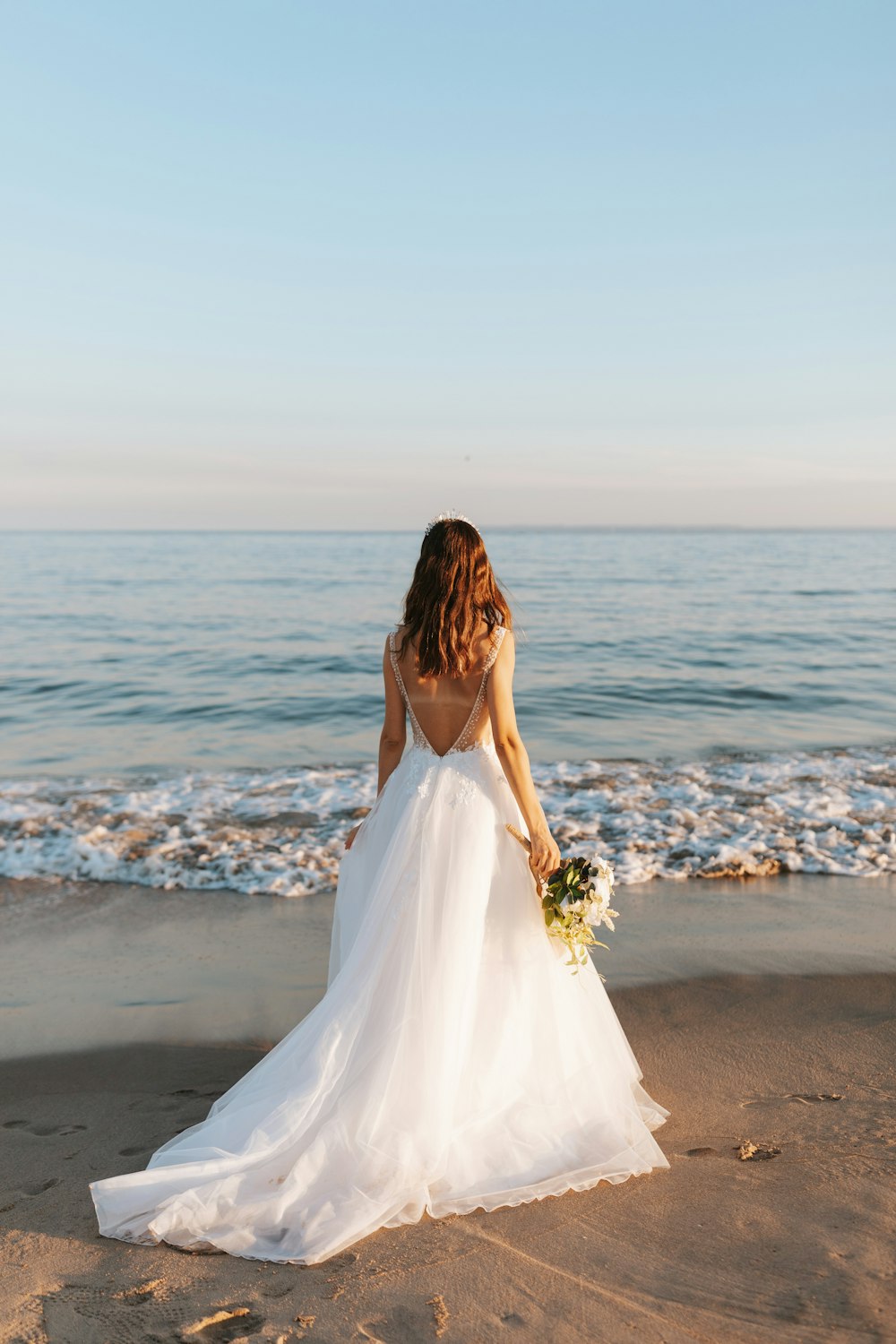 Mujer en vestido de novia blanco de pie en la playa durante el día