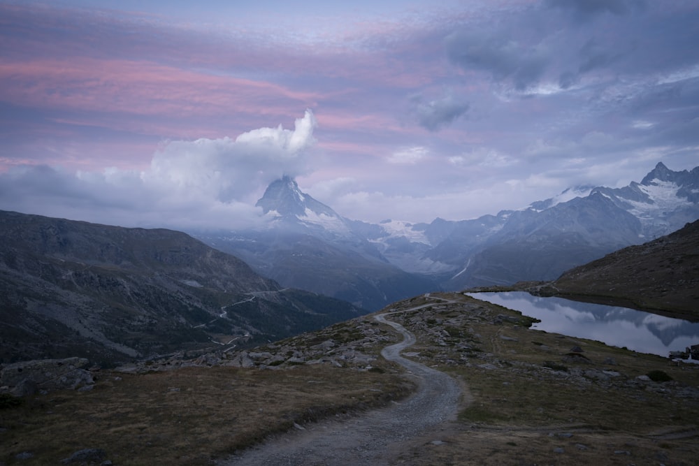 Route grise entre un champ d’herbe verte près de la montagne sous des nuages blancs pendant la journée