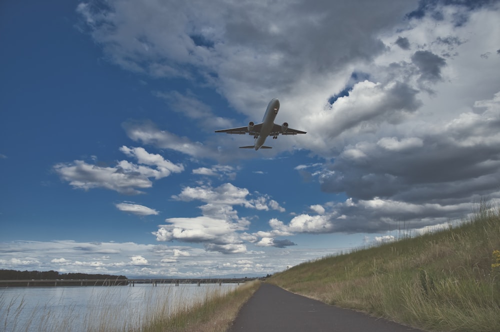 airplane flying over green grass field under blue and white cloudy sky during daytime