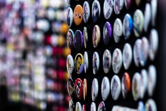 A collection of colorful round badges displayed in rows on a dark surface. Each badge has a unique design or image, ranging from patterns to illustrations. The background is softly blurred, emphasizing the sharp details of the badges in the foreground.