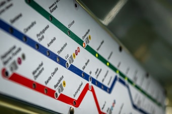 A close-up view of a subway or metro map showing multiple colored lines with station names written along each route. The map is angled, creating a diagonal visual perspective, and features colors such as green, blue, and red to distinguish different transit lines.
