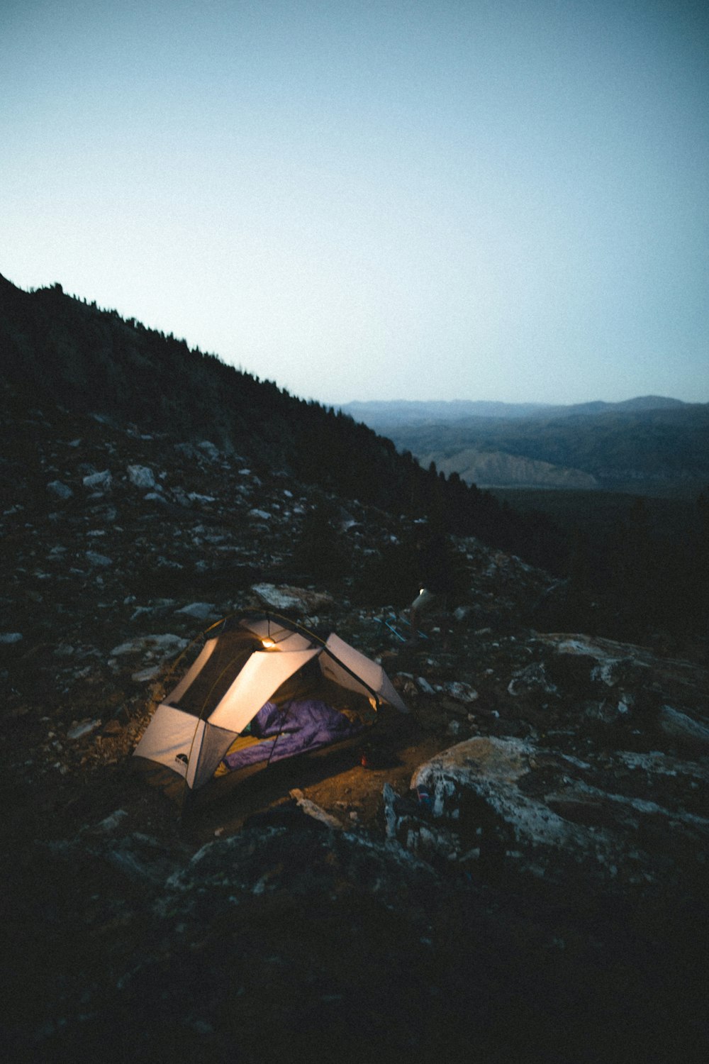 white and brown tent on rocky ground near trees during daytime