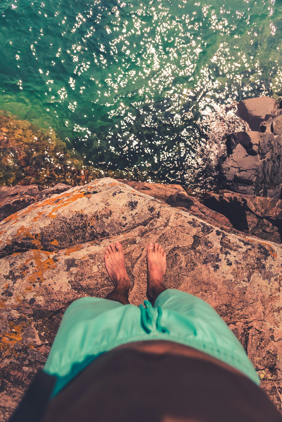 person in green pants sitting on rock near body of water during daytime