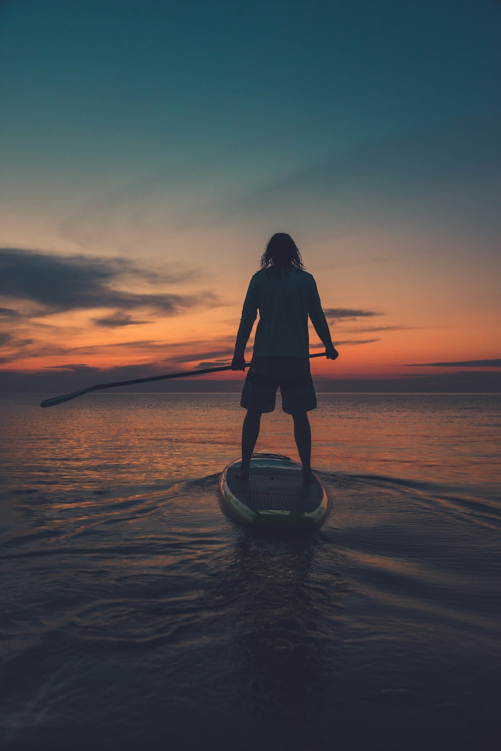 silhouette of woman standing on sea shore during sunset