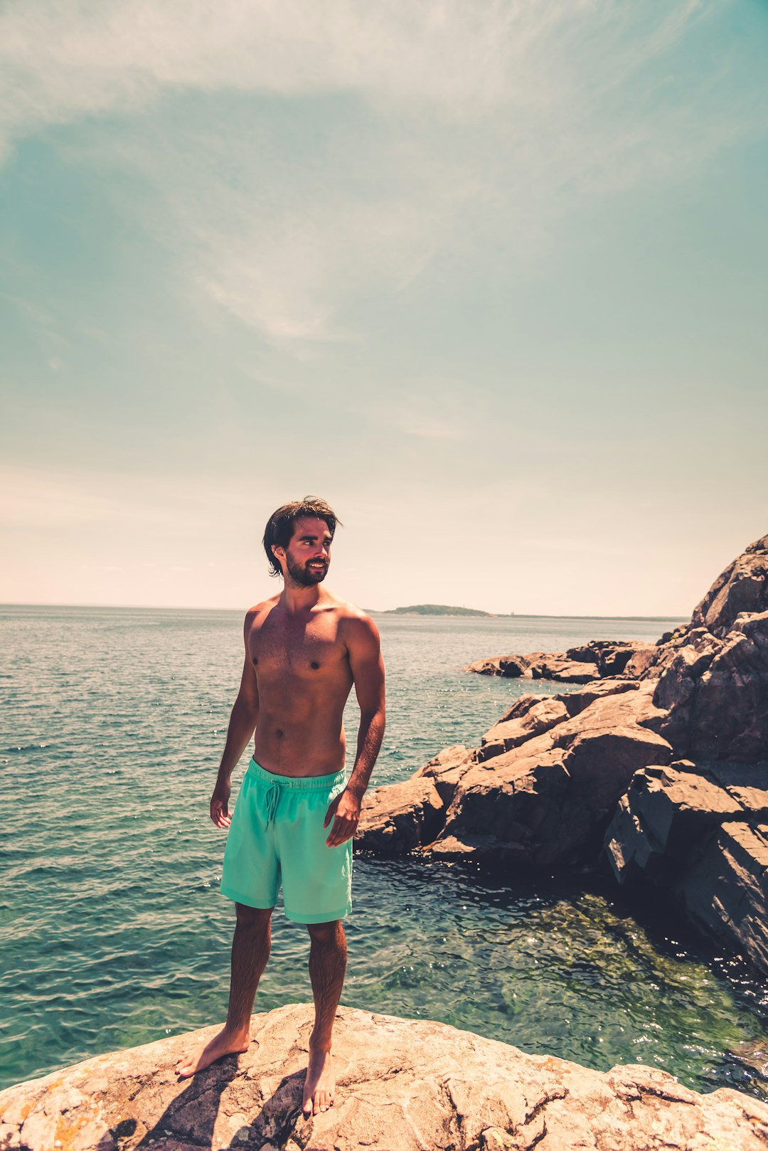topless man in green shorts standing on rocky shore during daytime