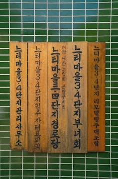 Vertical wooden plaques with Korean text mounted against a tiled green wall.