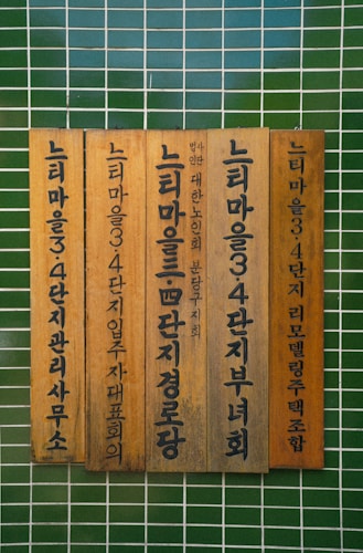 Vertical wooden plaques with Korean text mounted against a tiled green wall.