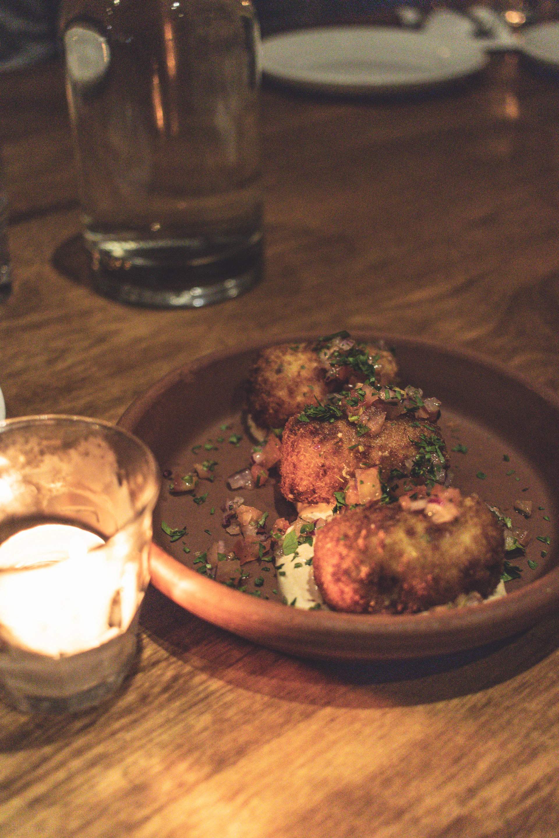 A warm, rustic wooden table set with a steaming bowl of creamy croquetas and a side of fresh salad, bathed in soft natural light.