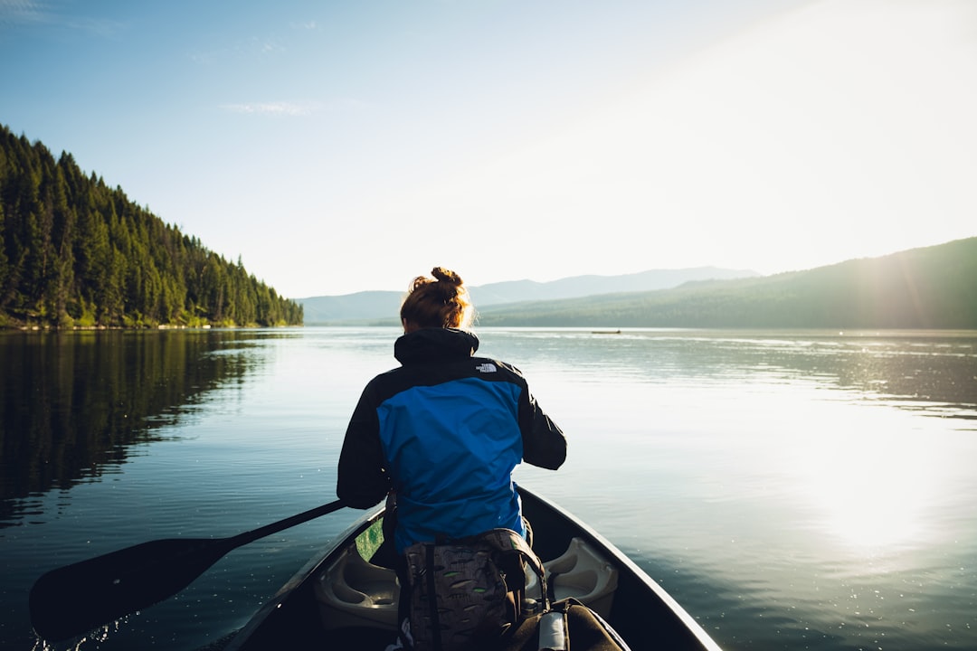 man in blue and black jacket sitting on boat on lake during daytime