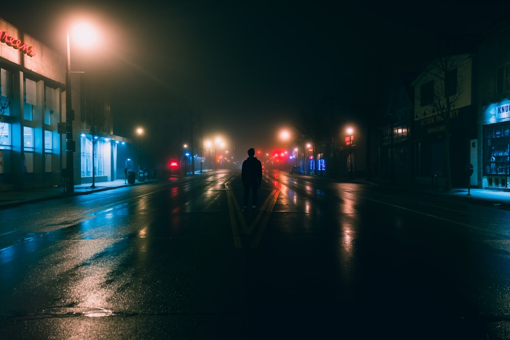 man in black jacket walking on sidewalk during night time