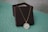 A gold chain necklace with a circular pendant that features a central teal-colored design encircled by clear stones. The necklace is draped over a dark brown jewelry box, both of which rest on a light teal surface. The background is a textured light blue-gray wall.