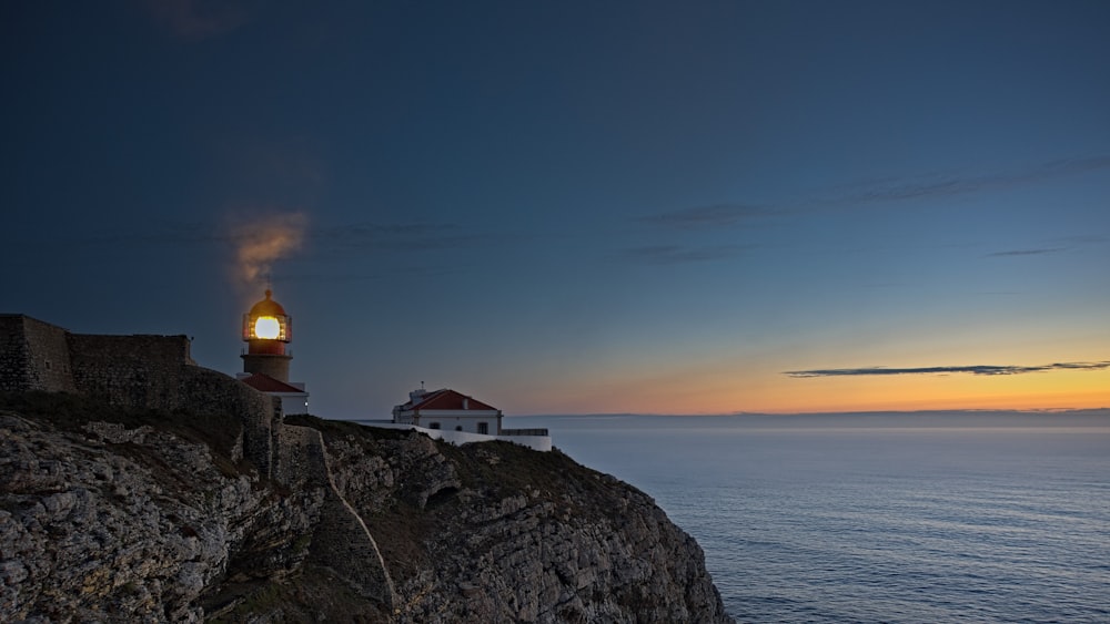 farol branco e marrom no penhasco à beira-mar durante o pôr do sol