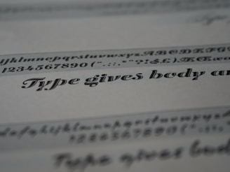 A close-up view of typeface samples printed on a sheet of paper. The text is in different styles and fonts, highlighting decorative and serif characteristics. The paper appears slightly angled, emphasizing the artistic nature of typography.