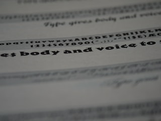 An image featuring a close-up view of text on a paper. The text includes various font styles and sizes, focusing on a bold and larger typeface in the middle. The image is blurred in certain areas, creating a depth of field effect.