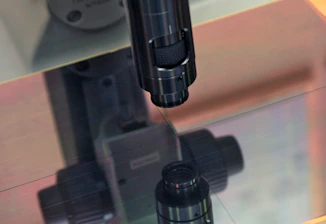 Close-up of a skilled technician inspecting a high-precision optical lens under bright lab lighting.