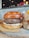 A juicy hamburger with a thick patty sitting on a slightly toasted bun. The burger features melted cheese beneath the patty, with a backdrop of a rustic interior with blurred lights and a cardboard container on the side.