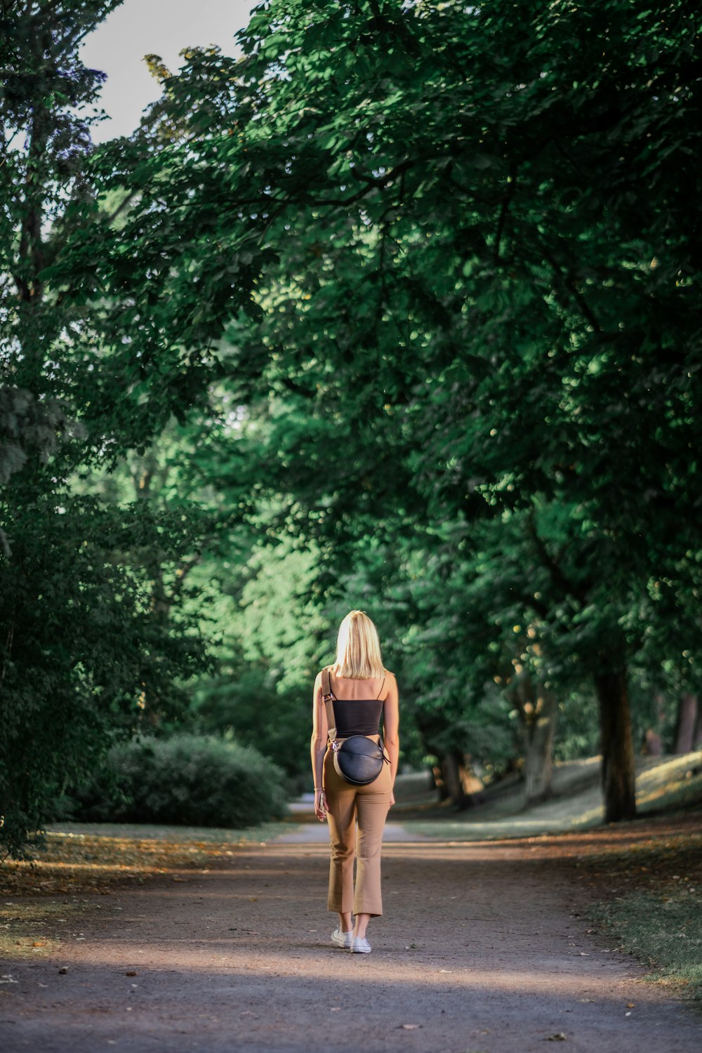 Donna in cappello da sole marrone che cammina sul sentiero tra gli alberi verdi durante il giorno