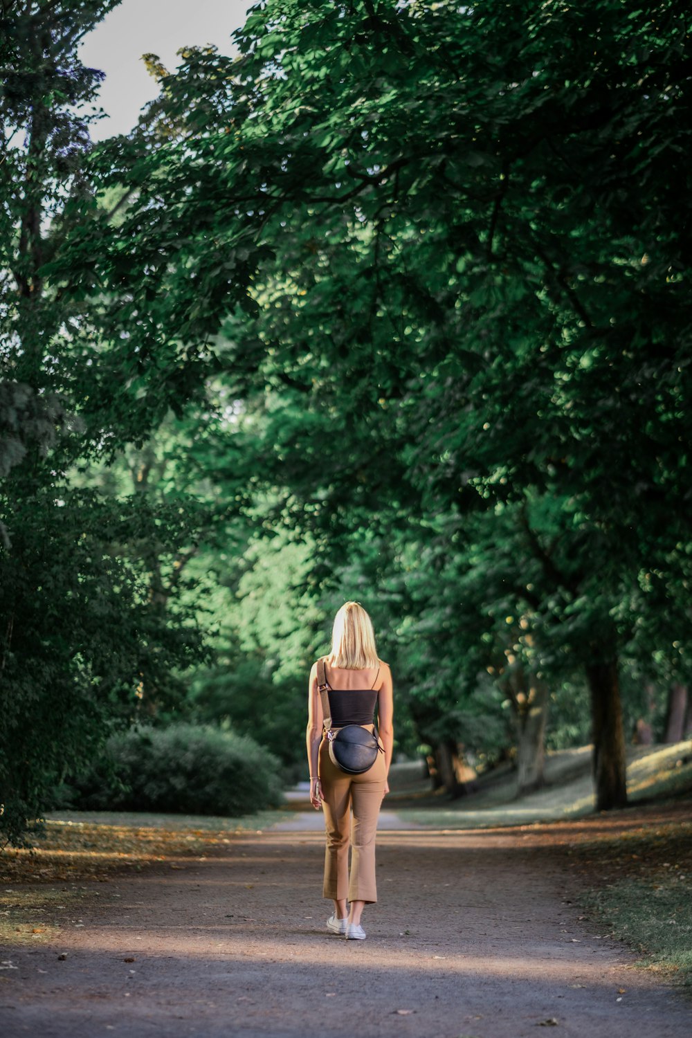 Mujer con sombrero marrón para el sol caminando por el camino entre los árboles verdes durante el día