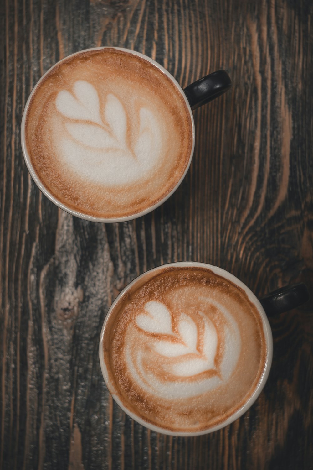 Dos tazas de capuchino sobre una mesa de madera