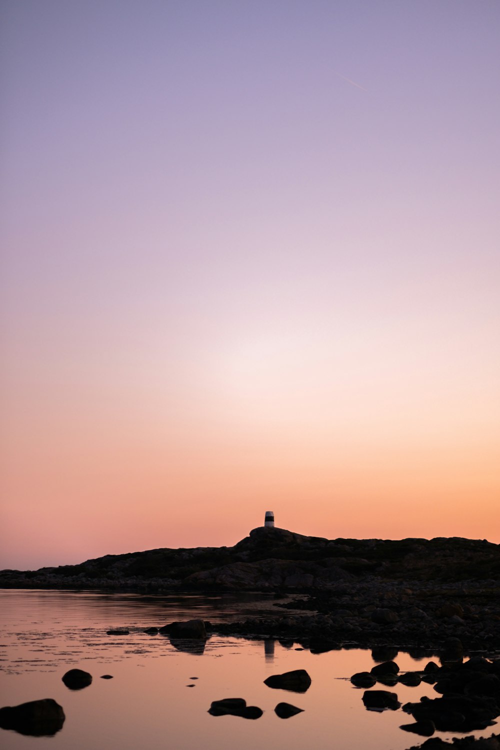 silhouette of person standing on rock formation near body of water during sunset