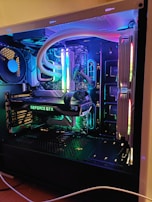 A well-organized and illuminated computer interior showcasing components like a GeForce GTX graphics card, illuminated RAM sticks, and other hardware. The setup features colorful LED lighting that enhances the aesthetic of the components and creates a vibrant visual appeal.