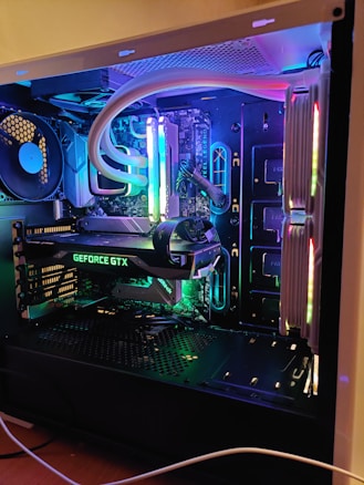 A well-organized and illuminated computer interior showcasing components like a GeForce GTX graphics card, illuminated RAM sticks, and other hardware. The setup features colorful LED lighting that enhances the aesthetic of the components and creates a vibrant visual appeal.