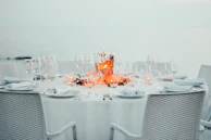 A fine dining table set outdoors with elegant beige linens and subtle candlelight by the beach.