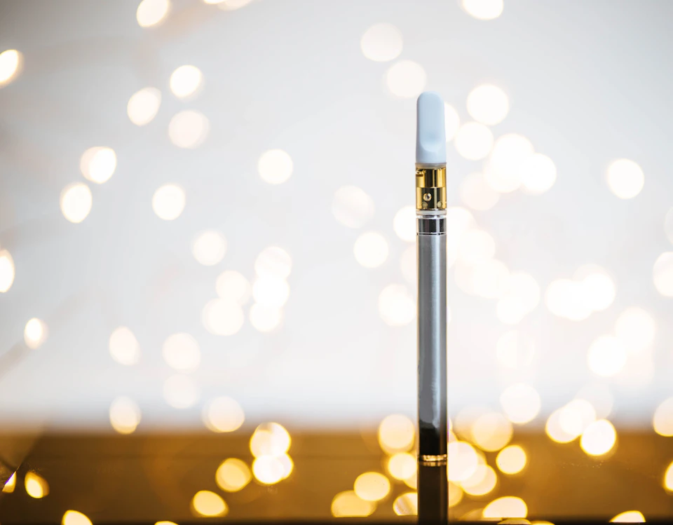Silver vaporizer with gold top and white base on wooden surface, slightly off-center