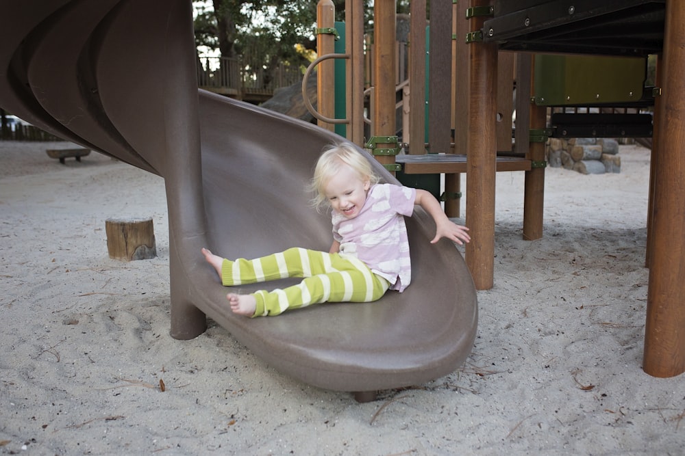 a little girl sitting on a slide in a playground