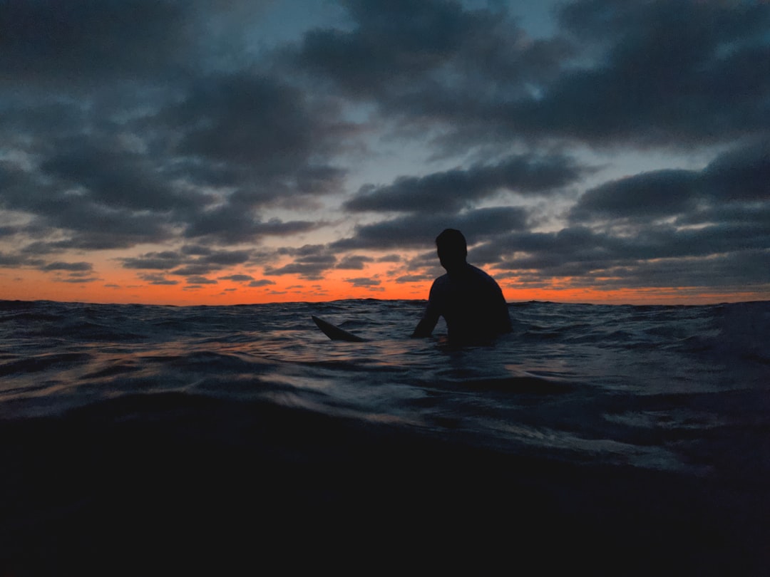 silhouette of man sitting on beach during sunset